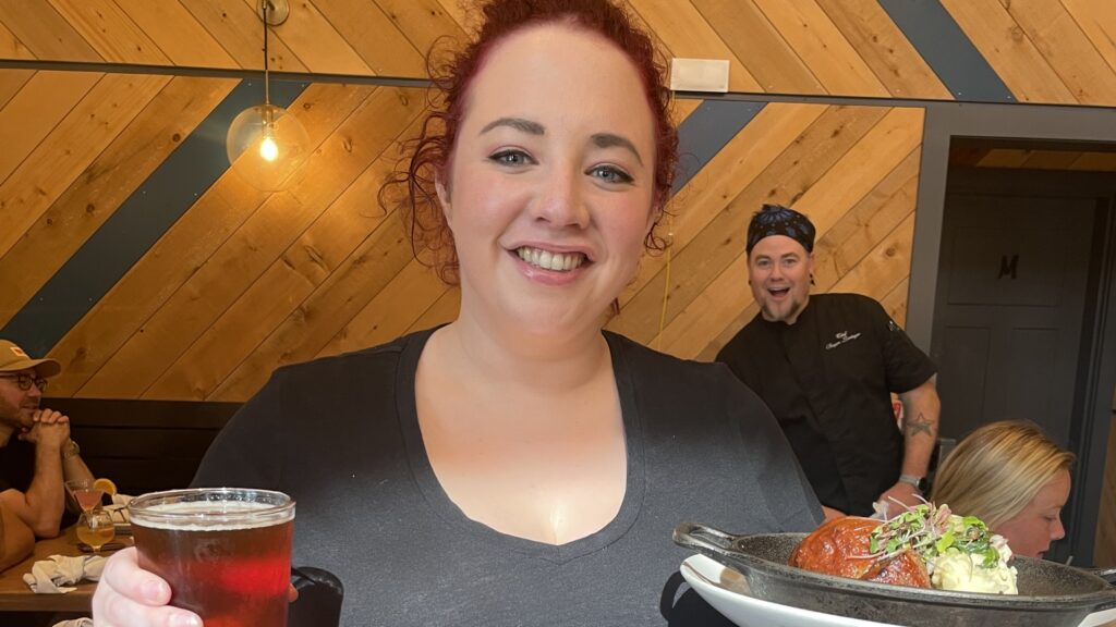 Server smiling with Chef Bryan photobombing the background